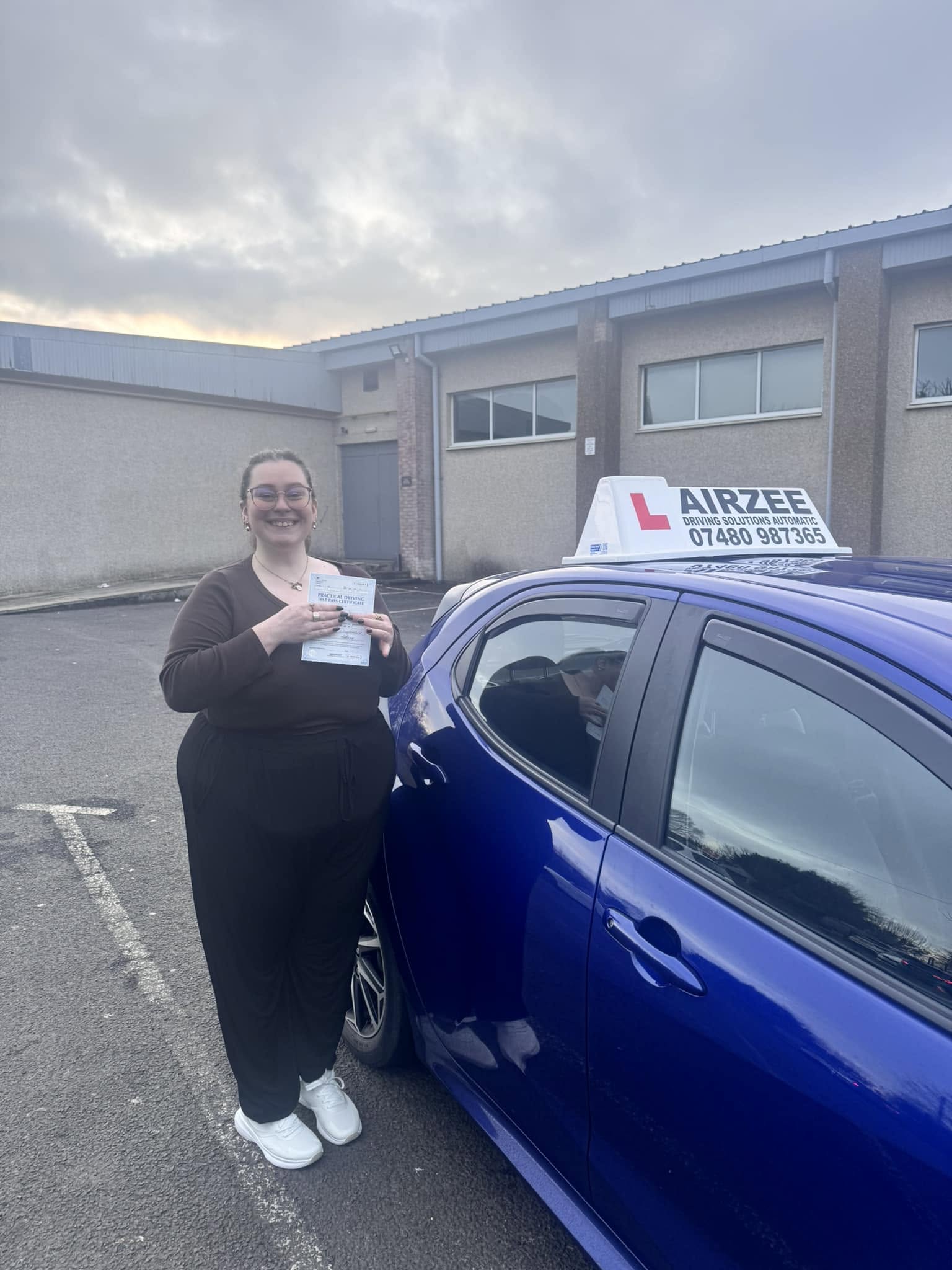 YorDrive learner celebrating with practical driving test pass certificate, blue Airzee training car