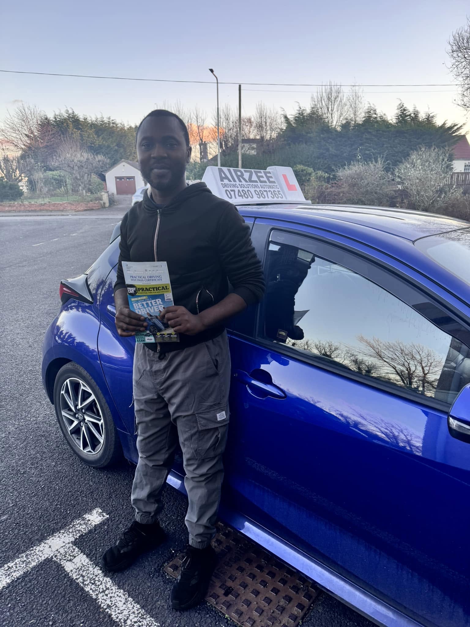 YorDrive learner celebrating with practical driving test pass certificate, blue Airzee training car