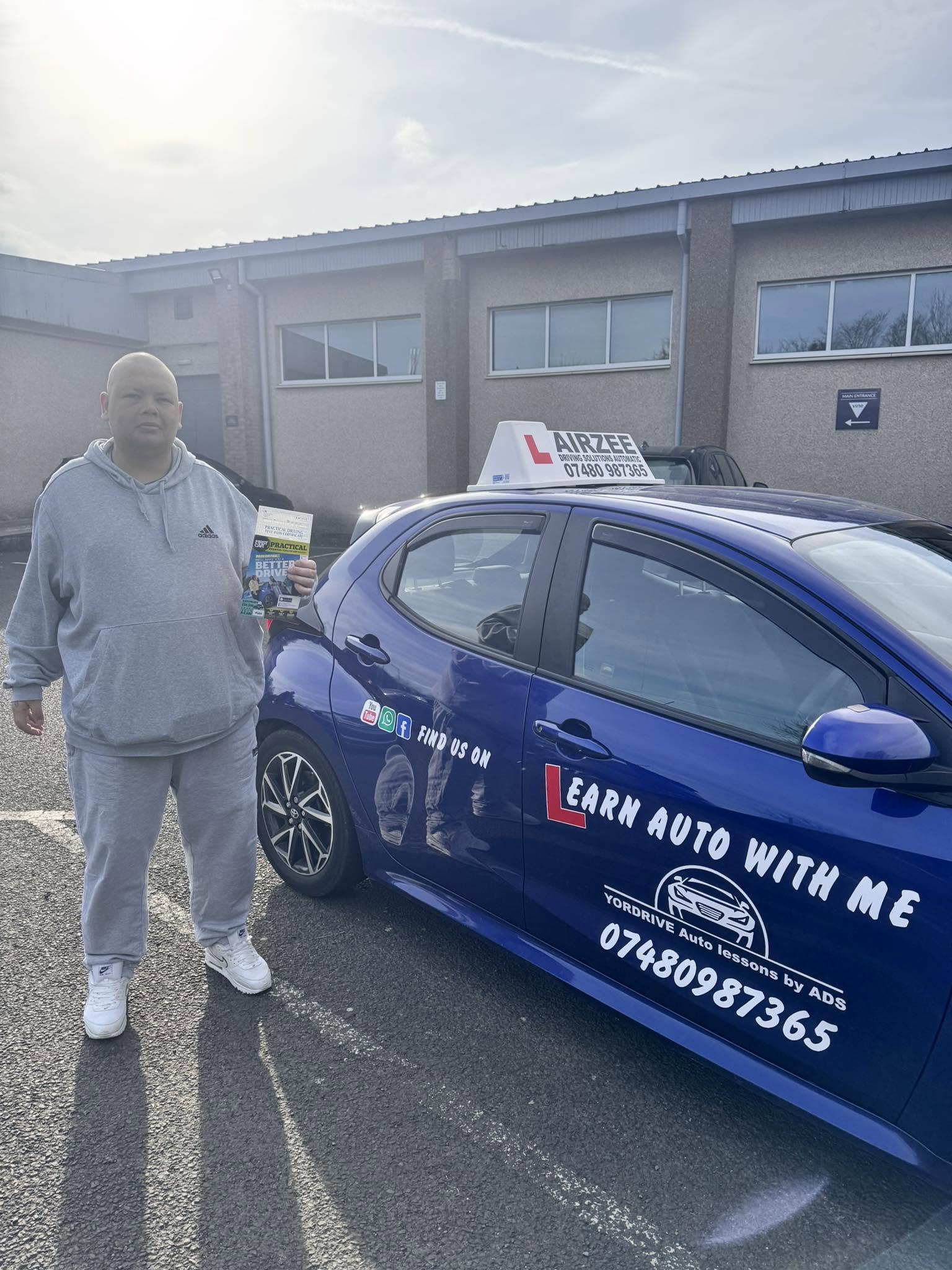 YorDrive learner celebrating with practical driving test pass certificate, blue Airzee training car